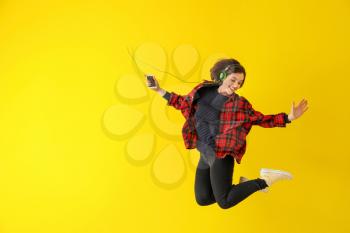 Jumping young woman with with headphones and mobile phone against color background�