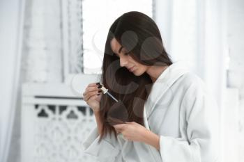 Beautiful young woman applying serum onto her healthy long hair at home�