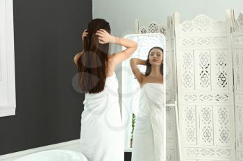 Beautiful young woman with healthy long hair looking in mirror at home�