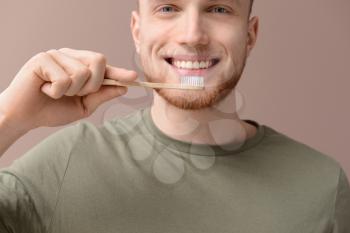 Young man cleaning teeth on color background, closeup�