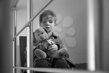 Homeless little boy with teddy bear sitting indoors�