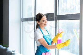 Female janitor cleaning window in office�
