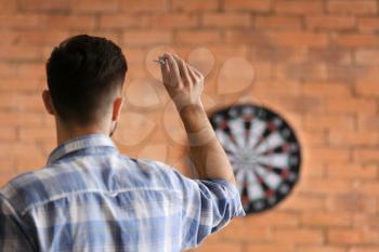 Young man playing darts indoors�
