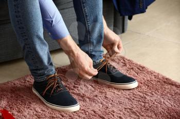 Young man putting on shoes in room�