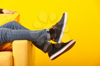 Stylish man in shoes sitting in armchair on color background�