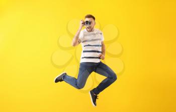 Jumping young man with photo camera on color background�