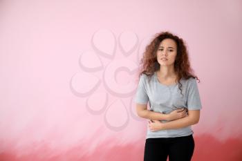 African-American woman suffering from abdominal pain on color background�