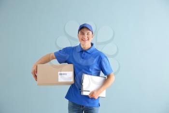 Delivery man with box and clipboard on color background�