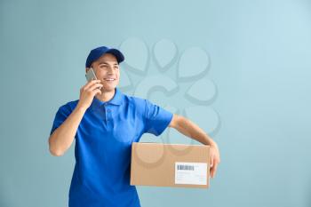 Delivery man with box talking by phone on color background�