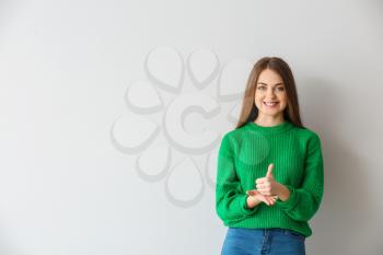 Young deaf mute woman using sign language on light background�