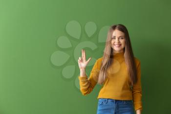 Young deaf mute woman using sign language on color background�