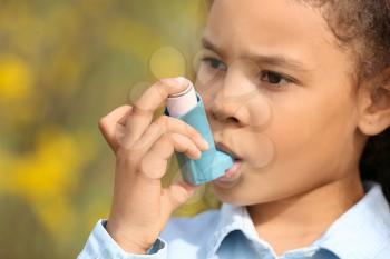 African-American girl with inhaler having asthma attack outdoors on spring day�