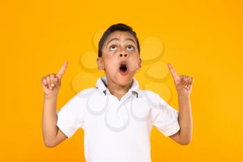 Portrait of cute little boy pointing at something on color background�