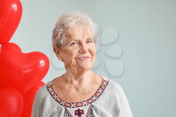 Portrait of senior woman with heart shaped air balloons on grey background�