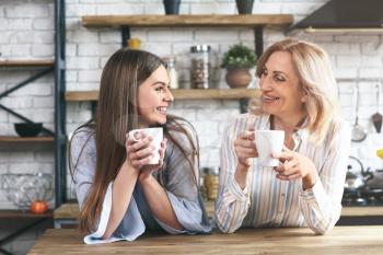 Happy mother and daughter drinking tea in kitchen at home�