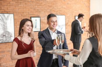 Waiter suggesting champagne to visitors of modern art gallery�
