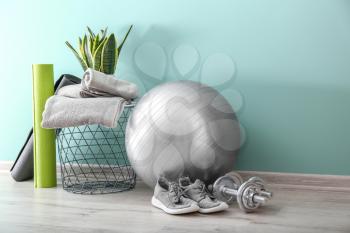 Set of sports equipment with fitness ball, towels and shoes near wall�