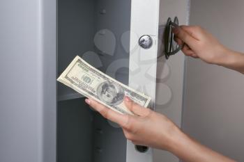 Woman with money opening modern safe, closeup�