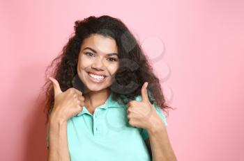 Portrait of happy African-American woman showing thumb-up gesture on color background�