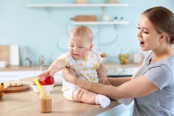 Mother feeding her little baby in kitchen at home�