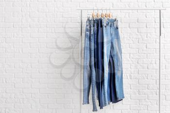 Clothes rack with different stylish jeans pants on white brick background�