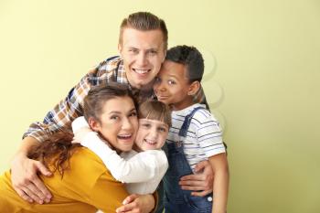 Happy couple with little adopted children on color background�