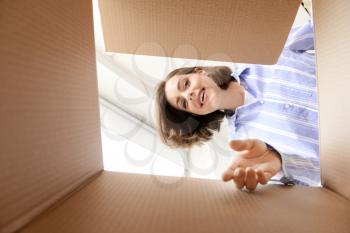 Young woman opening parcel at home, view from inside of box�