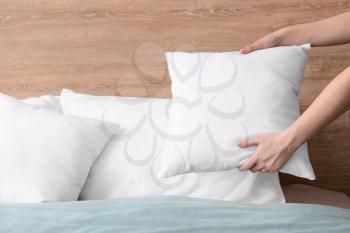 Woman fluffing soft pillows on bed�