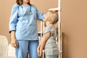 Female nurse measuring height of little girl in hospital�
