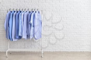 Rack with clothes after dry-cleaning near white brick wall�