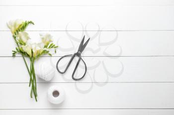 Beautiful freesia flowers, scissors and thread on white wooden table�