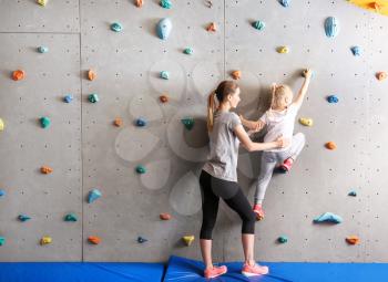 Instructor helping little girl to climb wall in gym�