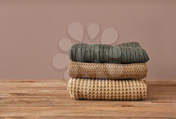 Stack of warm clothes on table against color background�