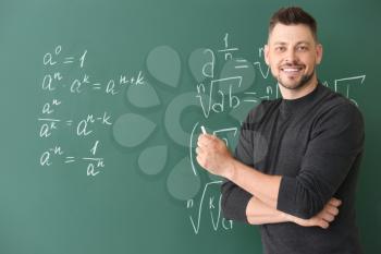 Handsome math teacher writing on blackboard in classroom�