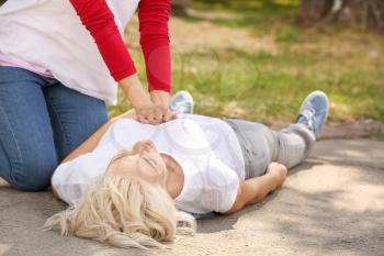 Female passer-by doing CPR on unconscious mature woman outdoors�