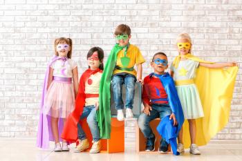 Cute little children dressed as superheroes near brick wall�