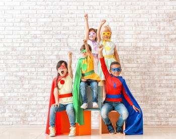Cute little children dressed as superheroes near brick wall�