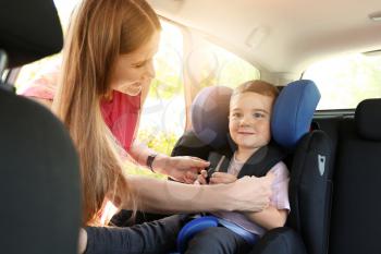 Mother buckling her little son in car seat�