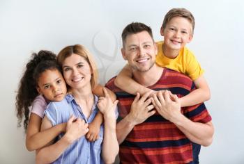 Happy couple with little adopted children on light background�