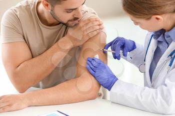 Doctor vaccinating young man in clinic�