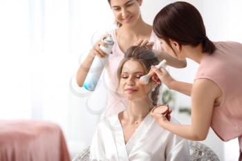 Professional makeup artist and hairdresser working with young bride at home�