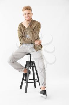 Stylish young man sitting on stool against white background�