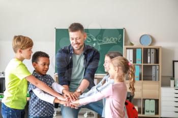Cute children with teacher putting hands together in classroom�