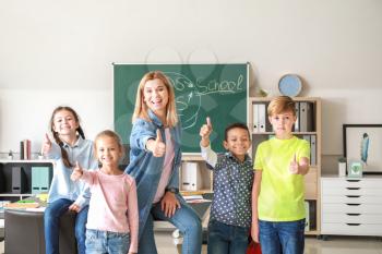 Cute children with teacher showing thumb-up gesture in classroom�