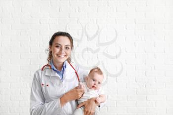 Pediatrician with cute little baby against white brick wall�