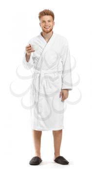 Handsome young man in bathrobe drinking coffee on white background�