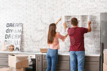 Young couple hanging shelf on wall in their new house�