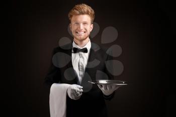 Handsome waiter with empty tray on dark background�