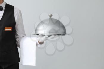 Handsome waiter with tray and cloche on light background�
