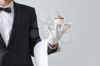 Handsome waiter with dessert on light background�